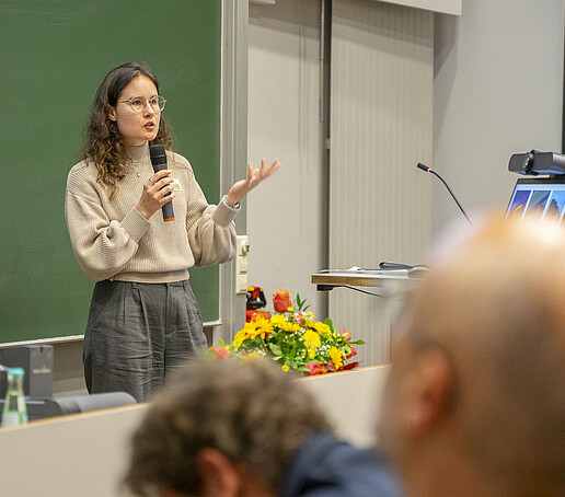 A woman speaks into a microphone in front of the audience.