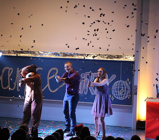 One person in a brown bear suit and three team members each explode a confetti cannon.