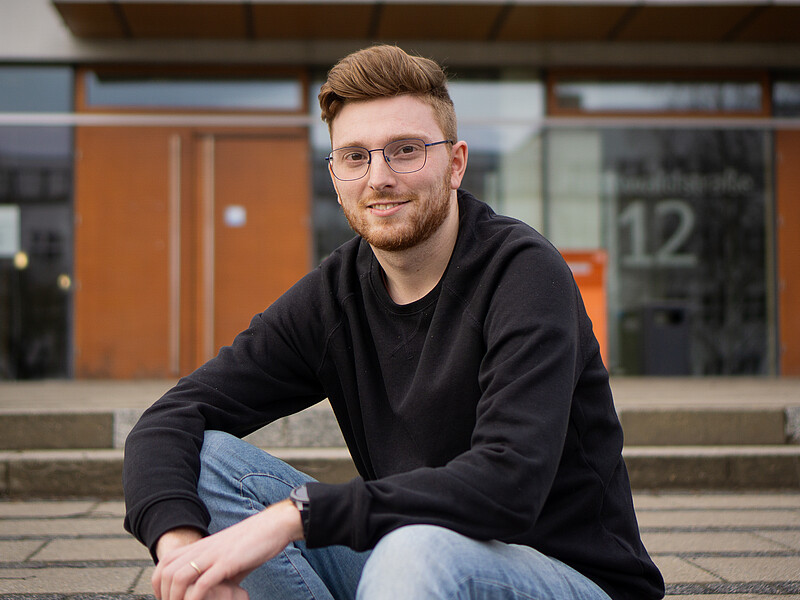 Johannes Krutz sitzt vor der Mensa auf den Treppenabsatz.