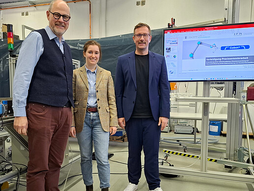 Three people are standing in the laboratory, next to a screen on which a graphic can be seen.