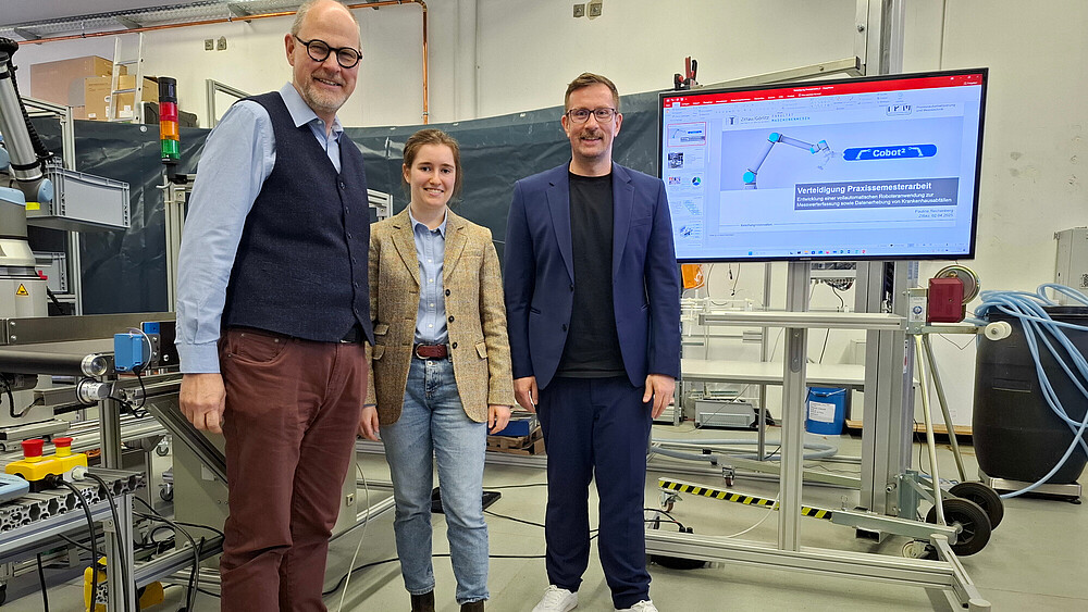Three people are standing in the laboratory, next to a screen on which a graphic can be seen.