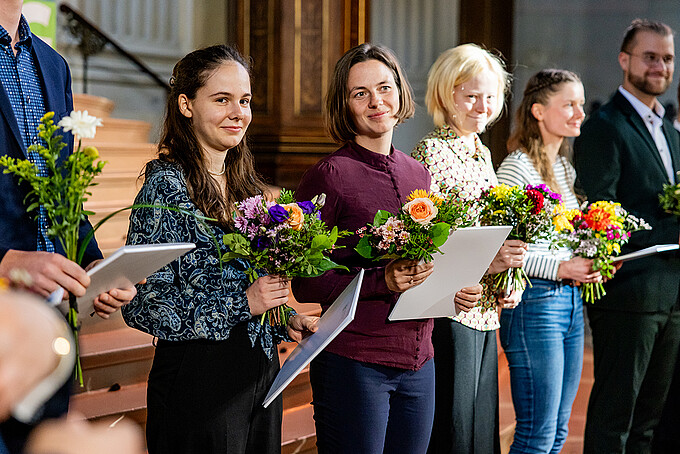 Several recipients of the Germany Scholarship are standing in the chancel of St. John’s Church, holding bouquets of flowers and certificates.