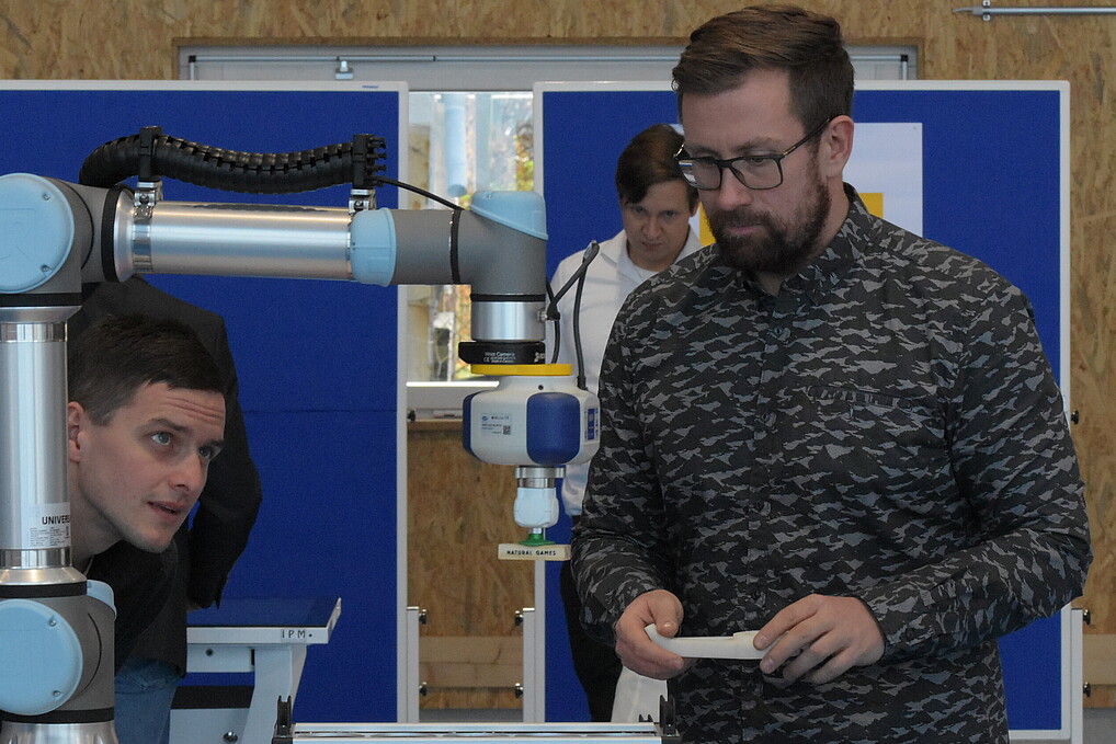 Two young men standing in front of a robot and looking at its functionality