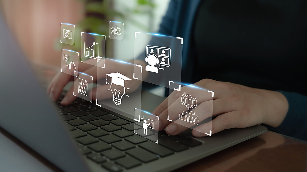 An edited image: two hands on the laptop keyboard, above them graphics like a light bulb with a graduate's hat, representing artificial intelligence.