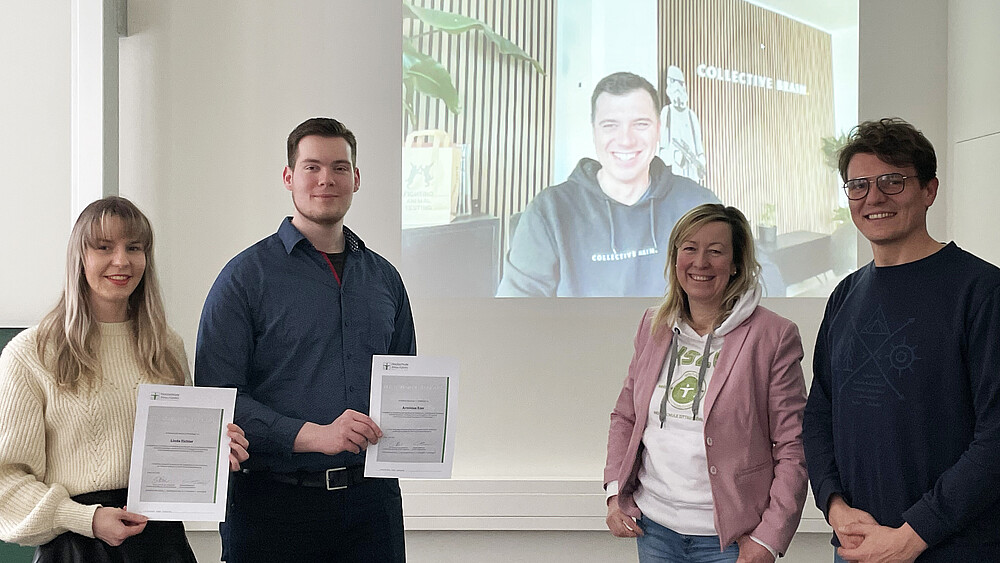 The Zuklos team and students stand in front of a wall onto which an agency employee is projected via webcam.