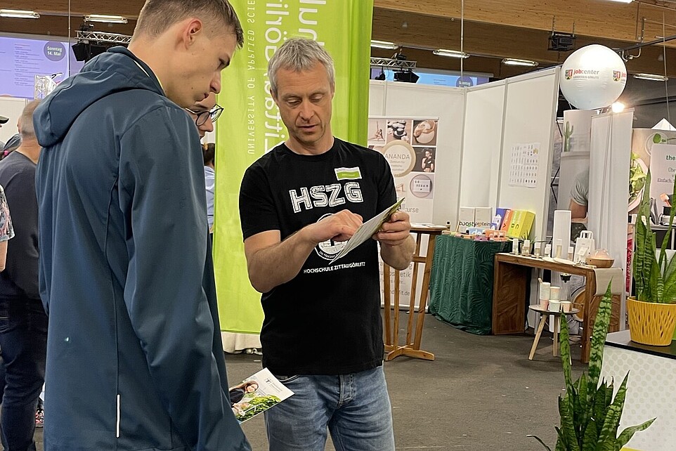 Ein HSZG-Mitarbeiter berät einen Studieninteressierten am Stand.