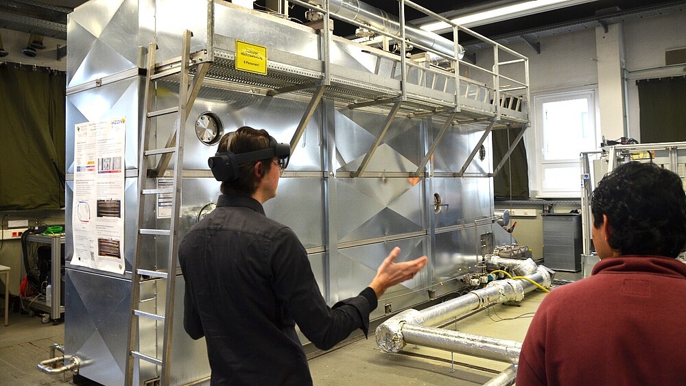 The two Mexican students Juan and Jorge (from left to right) during the live demonstration of their AR application. They are standing in front of a test facility, Juan is wearing VR glasses.