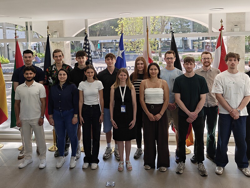 Prof. Dr.-Ing. Patricia Stang (1st row, 4th from left) from the Faculty of Electrical Engineering and Computer Science with students at the Tecnológico de Monterrey stand next to each other in the foyer of a building in front of glass windows for a group photo.