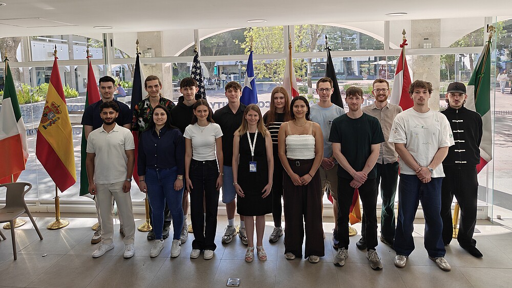 Prof. Dr.-Ing. Patricia Stang (1st row, 4th from left) from the Faculty of Electrical Engineering and Computer Science with students at the Tecnológico de Monterrey stand next to each other in the foyer of a building in front of glass windows for a group photo.