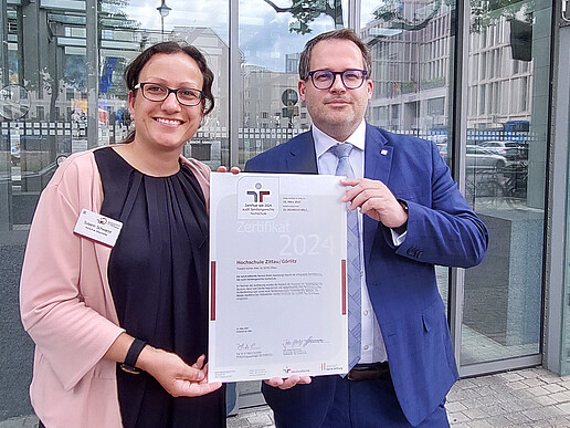Susann Schwarze und der Rektor halten das Zertifikat zur familiengerechten Hochschule in die Höhe.