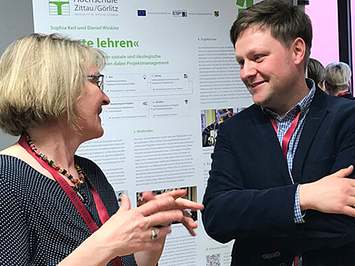 Two people stand in front of a poster and exchange ideas.