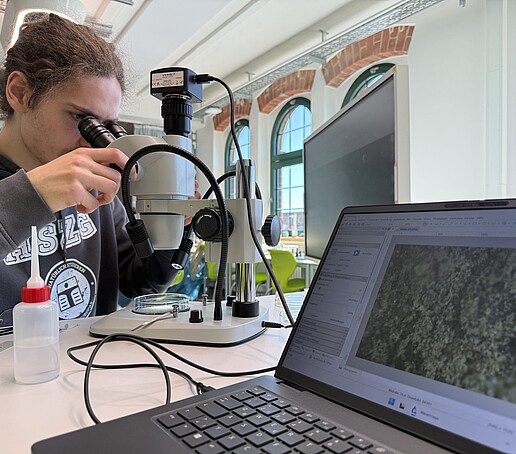 Ein junger Mann schaut durch ein Mikroskop.