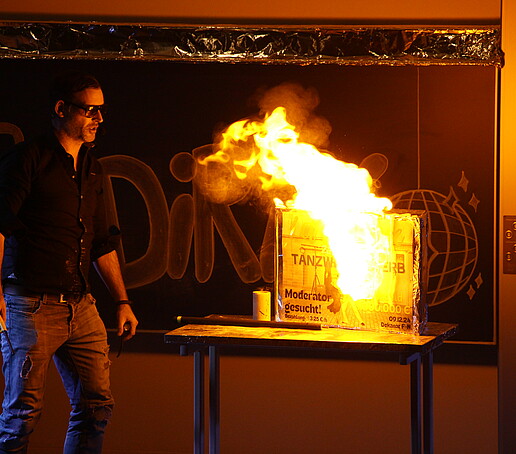 One person conducts a flaming experiment on stage in the dark.