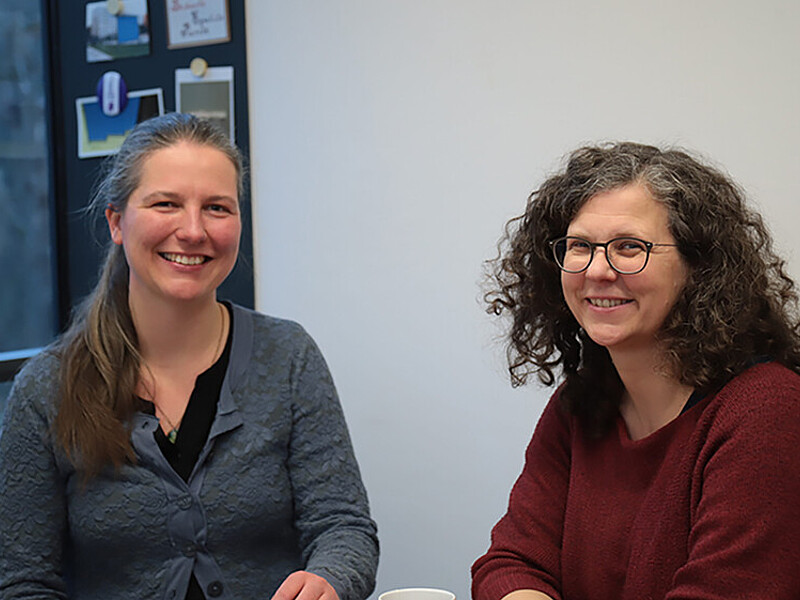 Sabine Bublitz und Professorin Schulze sitzen am Tisch und lächeln in die Kamera.