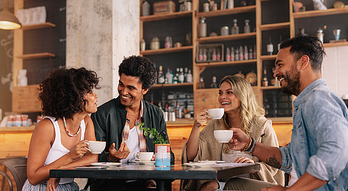 Vier junge Menschen mit unterschiedlicher Nationalität sitzen an einem Tisch und trinken aus Tassen