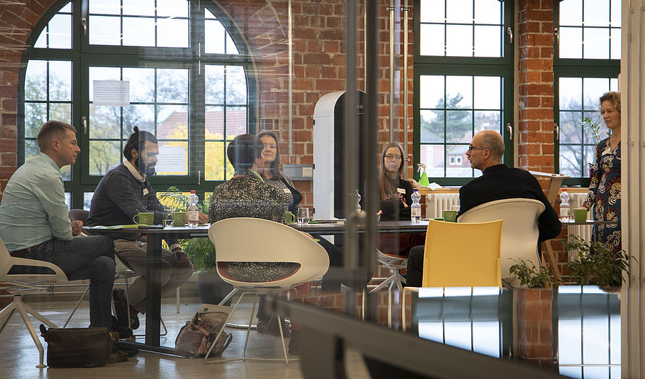 Foto: Sven Müller Gruppe sitzt am Tisch und diskutiert mit Dozentin.