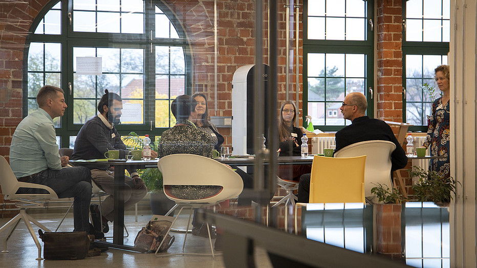 Foto: Sven Müller Gruppe sitzt am Tisch und diskutiert mit Dozentin.