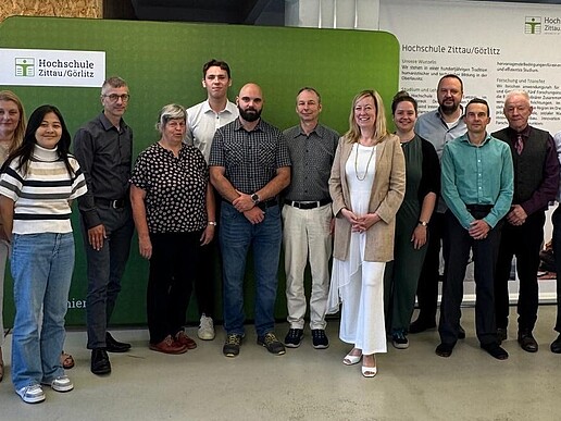 Vertretende der HSZG und Infineon Technologies stehen im Celsiuz zum Gruppenbild nebeneinander vor einer grünen Pressewand und einem HSZG-Rollup.