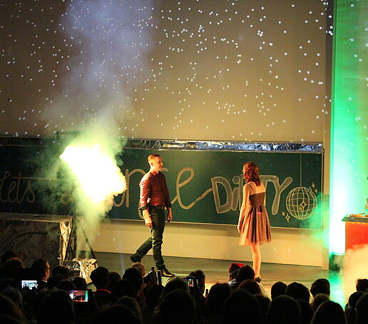 A dancing couple approach each other on stage. Fog can be seen all around them.