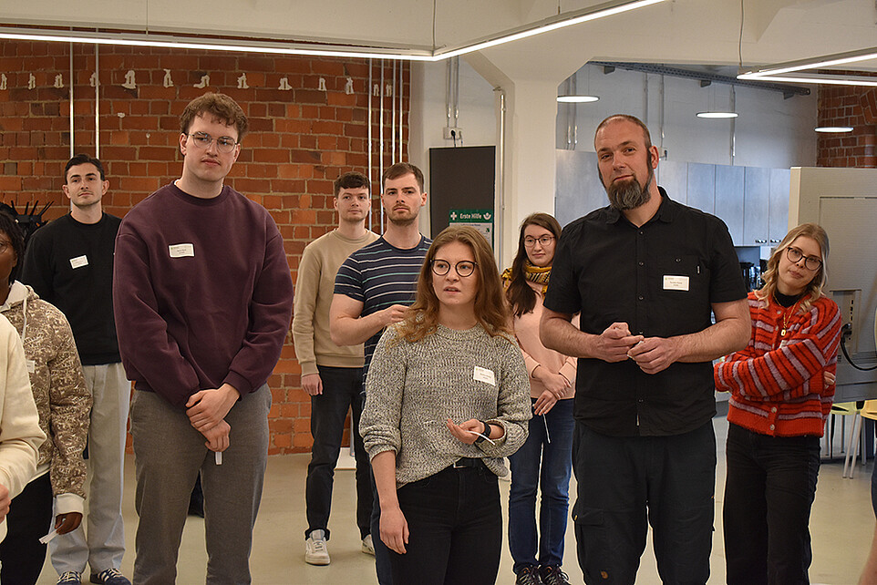 Workshop participants stand next to each other in the Celsiuz workroom and discuss a task.