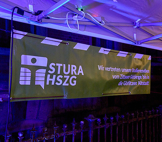 A green and white StuRa banner hangs from a pavilion.