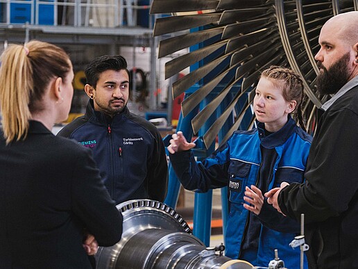 Sandeep and Alina stand in front of a turbine in a factory hall and talk to the KIA coordinator at HSZG and a Siemens employee.