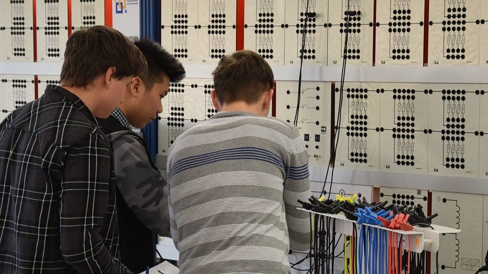 Drei Schüler stehen im Elektrotechnik-Labor und bereiten ein Experiment vor.