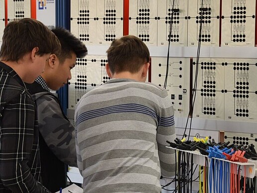 Drei Schüler stehen im Elektrotechnik-Labor und bereiten ein Experiment vor.