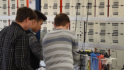 Drei Schüler stehen im Elektrotechnik-Labor und bereiten ein Experiment vor.