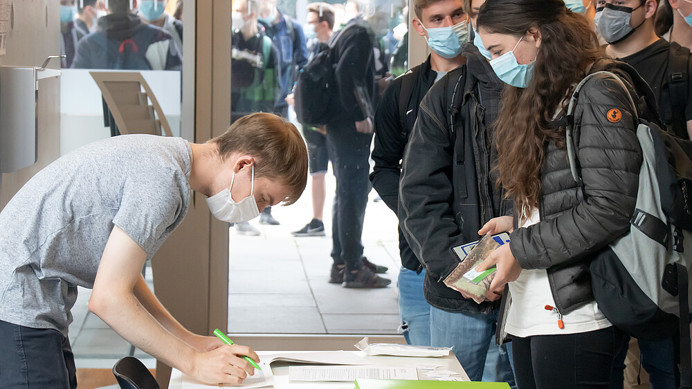 Studierende stehen vor einem Tisch und schreiben sich für die Come-In-Veranstaltung ein.