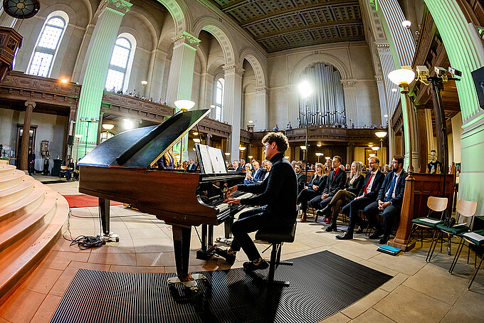 Samuel Wagner is sitting at the grand piano and playing during the musical degree ceremony finale.