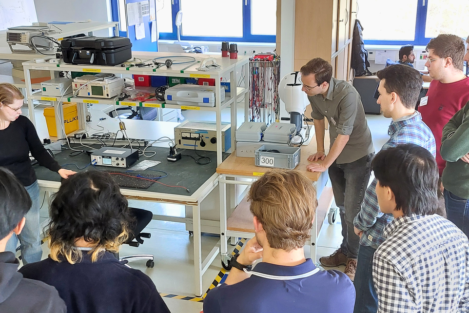 Mehrere Personen stehen im Halbkreis und betrachten einen Versuchsstand