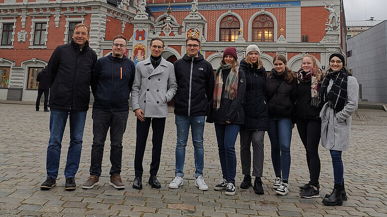 Prof. Jörg Kroschel mit seinen Studierenden vor einem Gebäude in der Innenstadt von Riga.