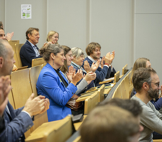 The audience sits on the rows of seats applauding.