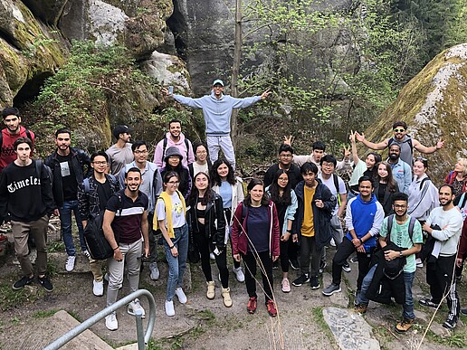Eine Gruppe internationaler Studierender steht vor einer Gesteinsformation des Berges Oybin und lächelt in die Kamera.