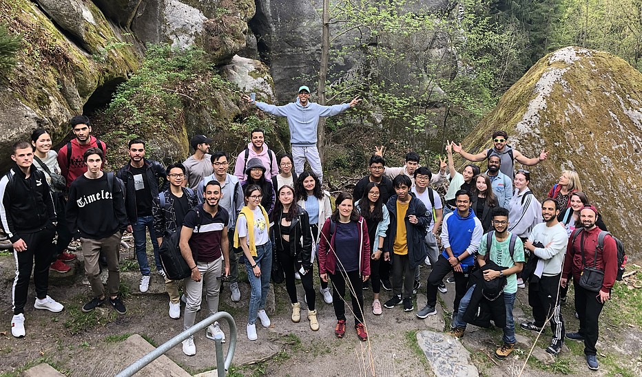 Foto: HSZG Eine Gruppe internationaler Studierender steht vor einer Gesteinsformation des Berges Oybin und lächelt in die Kamera.