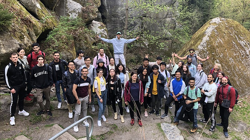 Eine Gruppe internationaler Studierender steht vor einer Gesteinsformation des Berges Oybin und lächelt in die Kamera.