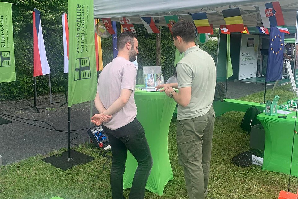Two men are standing at the green bar table writing a postcard.