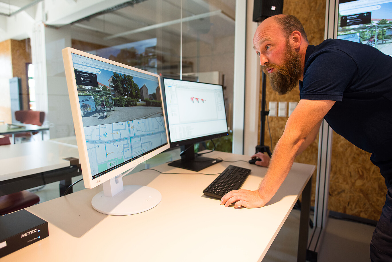 A research assistant leans over the keyboard of his desk and looks at a monitor.