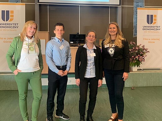 Vier Vertretende der HSZG stehen in einer mit Roll-ups geschmückten Halle nebeneinander und lächeln in die Kamera.