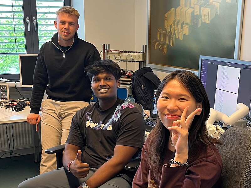 Drei ausländische Studierende sitzen in einem Büro und lächeln in die Kamera.