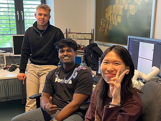 Drei ausländische Studierende sitzen in einem Büro und lächeln in die Kamera.