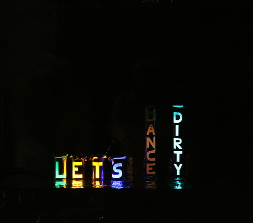 In the dark, the words Let's Dance Dirty glow in colorful letters.