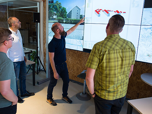 Four project team members stand in front of a large digital screen. Martin Herling points to a statistic.