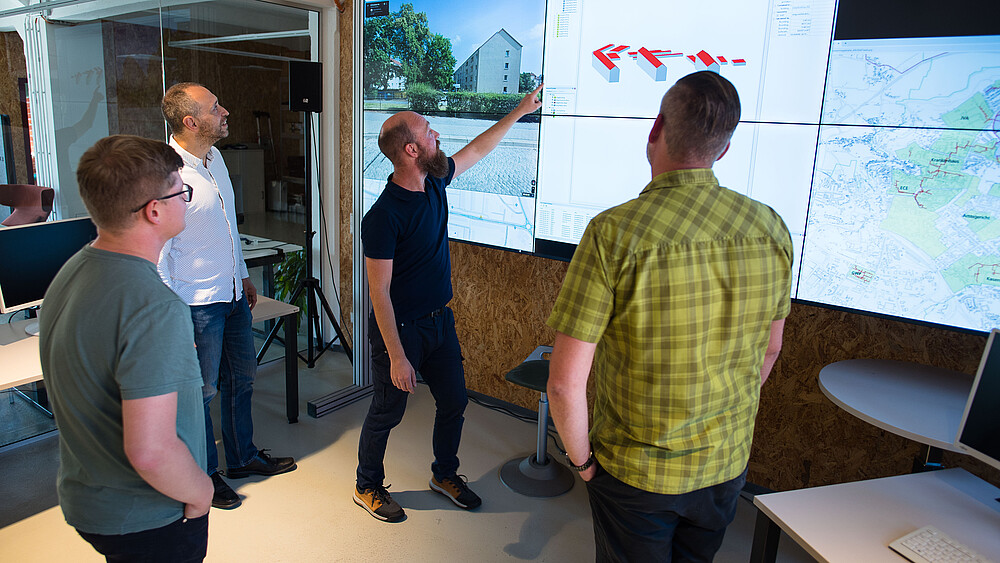 Four project team members stand in front of a large digital screen. Martin Herling points to a statistic.
