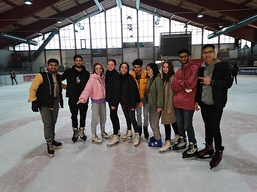 A group of international students stand on the ice surface in the Jonsdorf ice rink and smile at the camera.