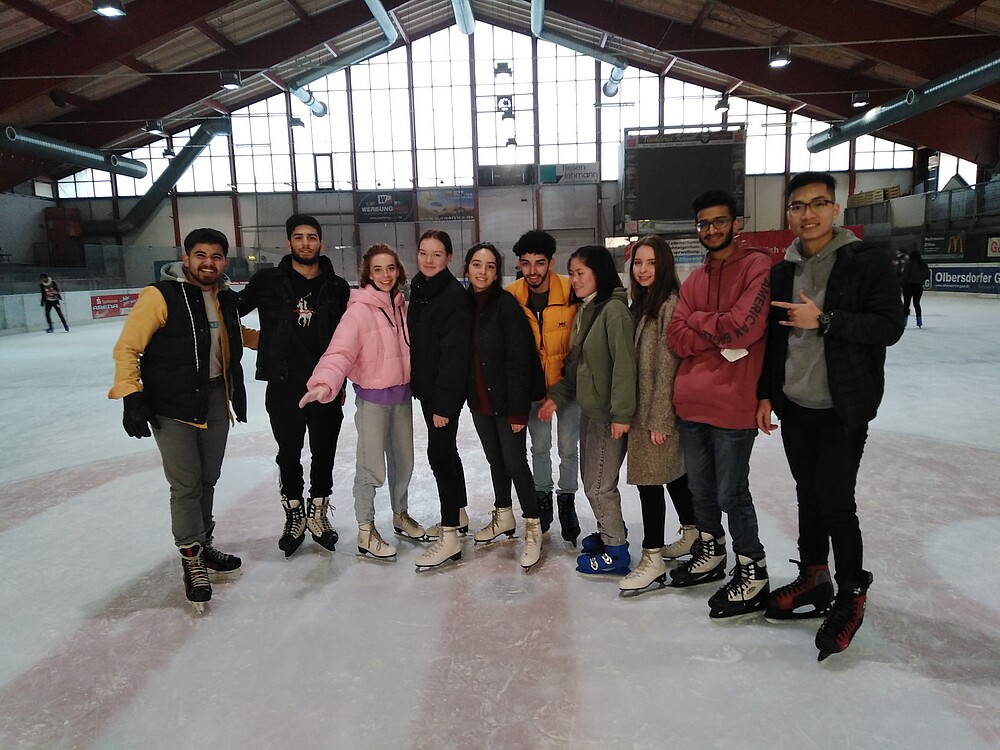 A group of international students stand on the ice surface in the Jonsdorf ice rink and smile at the camera.