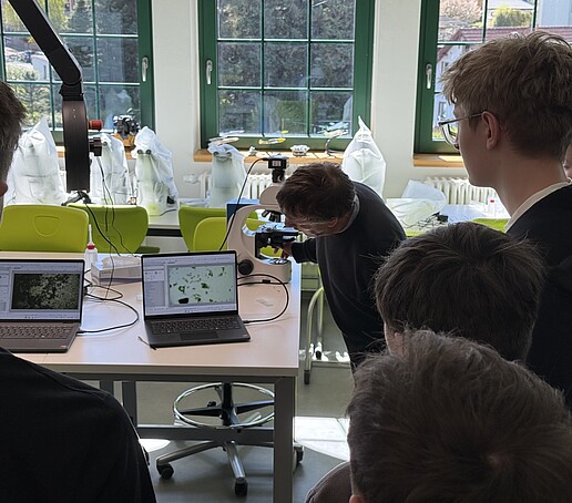 Dr. Fester erklärt Schülern etwas anhand eines Mikroskops.