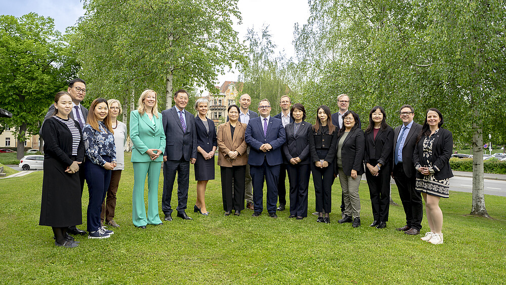 Mongolian guests and university members stand on the lawn next to the canteen and smile at the camera.