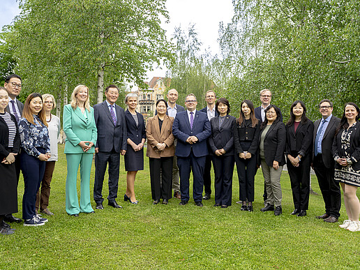 Mongolian guests and university members stand on the lawn next to the canteen and smile at the camera.